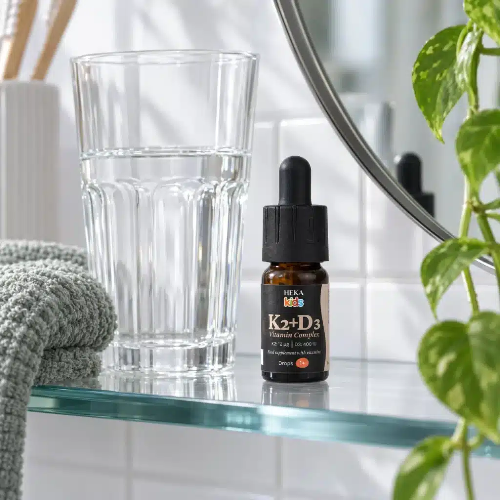 HEKA Kids K2+D3 Drops on a bathroom shelf with a glass of water